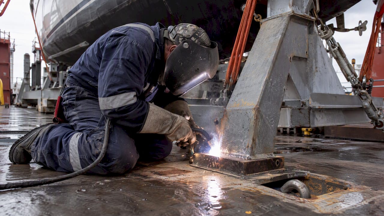 Welder fastening yacht cradle to ship deck